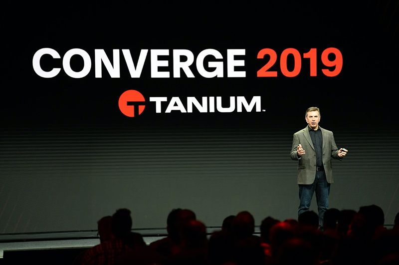 CONVERGE 2019 stage setup with speaker and large screens displaying Tanium messaging