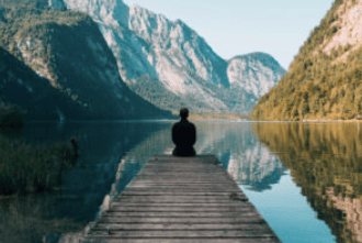 Person sitting on dock overlooking mountain lake and forested landscape