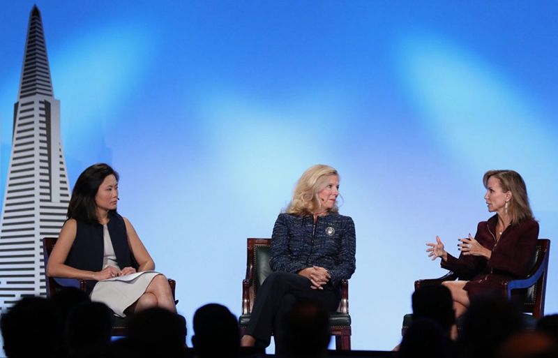 Three women in a panel discussion on a stage with a city skyline backdrop
