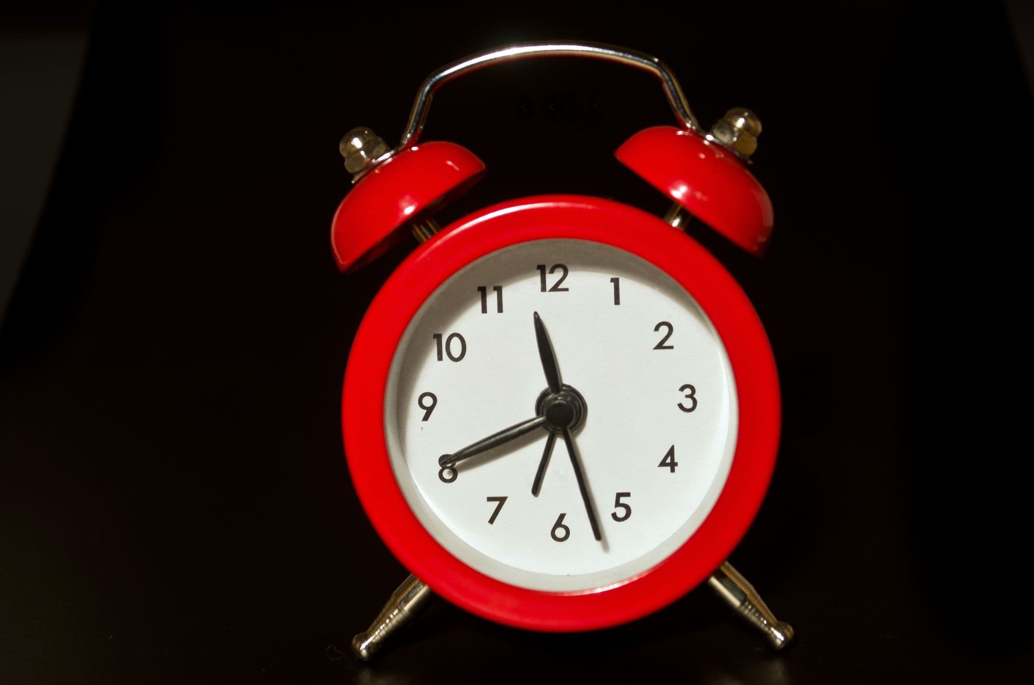 A bright red alarm clock stands against a black background--the hands on the clockface show the time is 11:41.