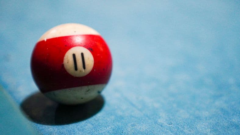A white billiard ball with a wide red band and marked with the number 11 sits on a pool table.