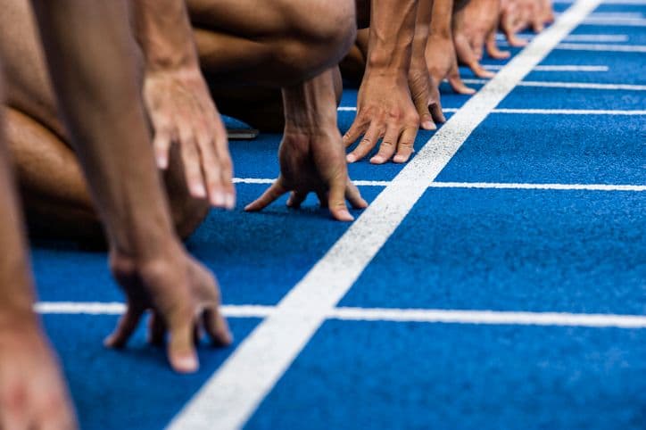 A closeup photo of runners' hands gripping the ground at the starting line of a race.
