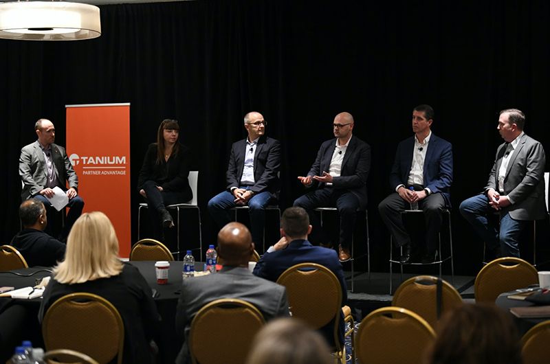 Panel of 6 people seated on stage at Tanium conference with logo backdrop