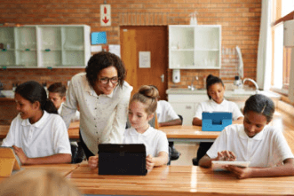 Teacher helping students at desk with tablet computer in classroom