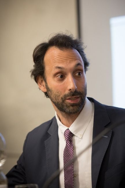 Headshot of a man with beard wearing a dark suit and purple patterned tie