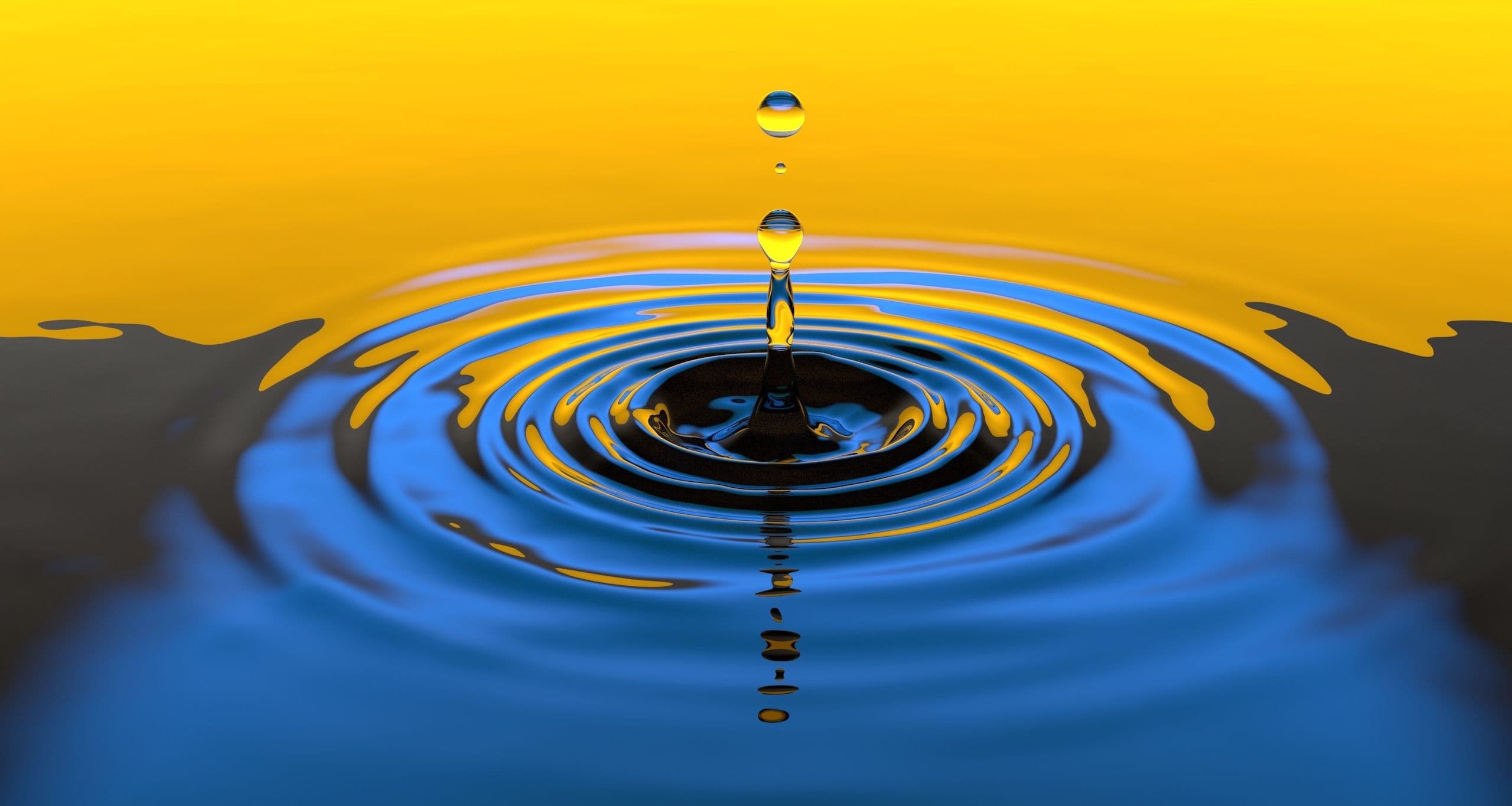 A water droplet falling in a lake creates circular outward ripples of blue and gold.