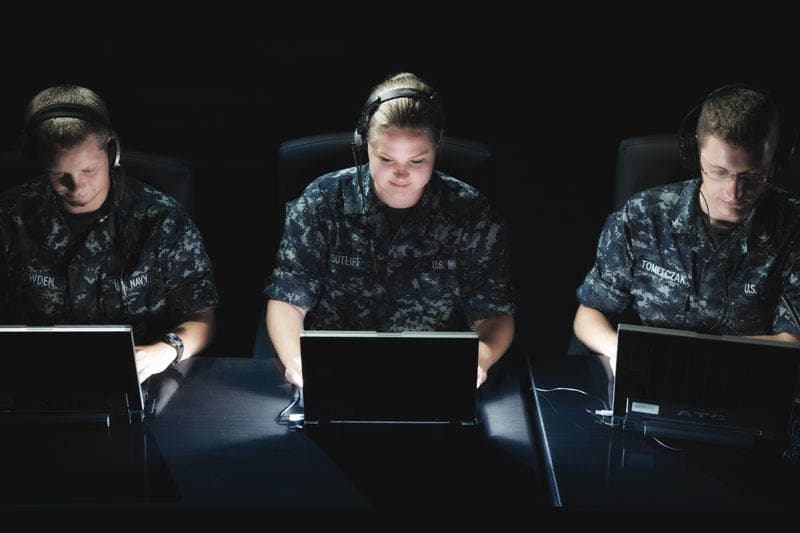 Three Navy personnel in uniforms working at computers