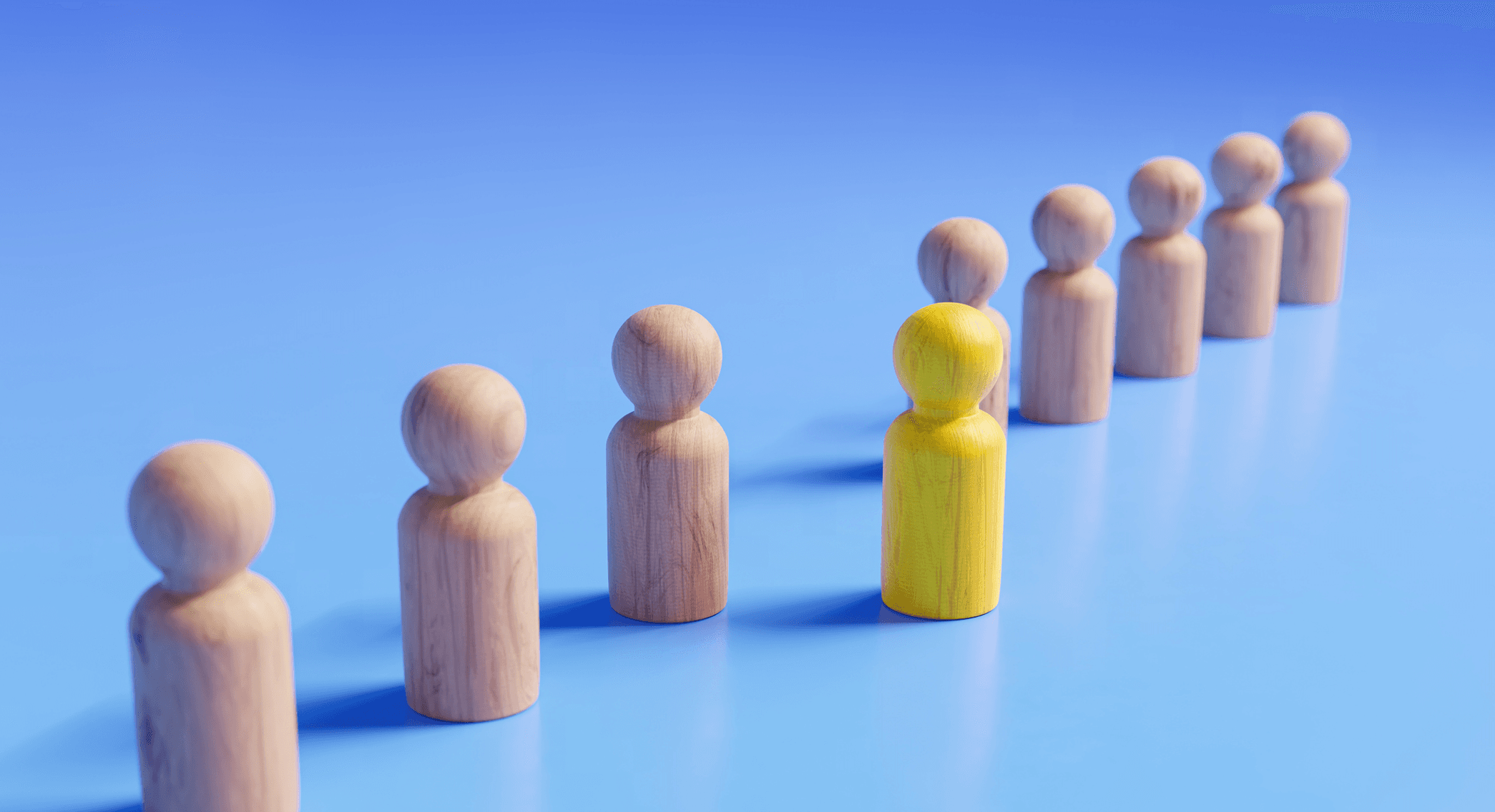Wooden figures stand in a diagonal line against a blue field, with one yellow figure one step forward.