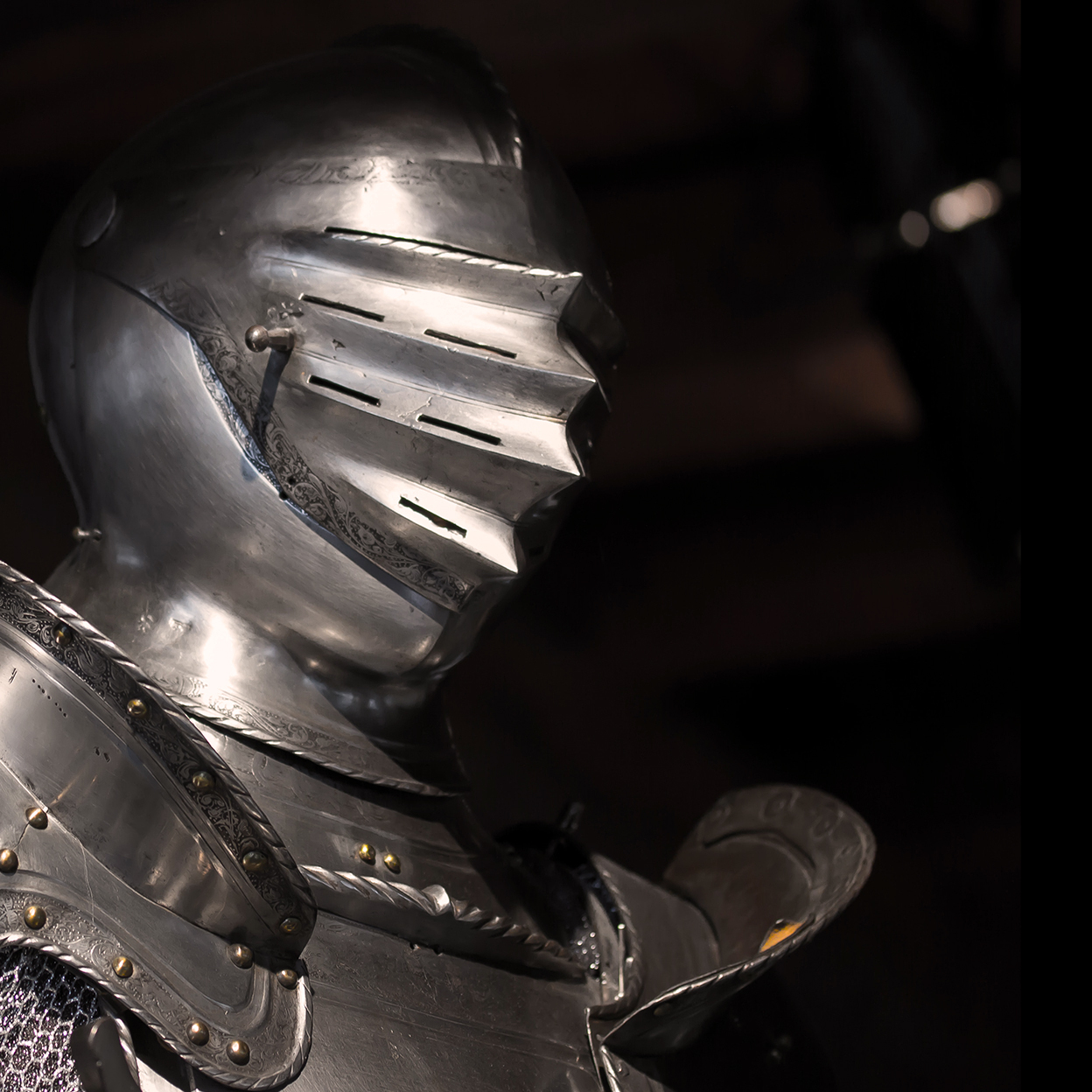 A photo of the head and shoulders of a knight in silver armor with a helmet bearing thin slits over the eyes.