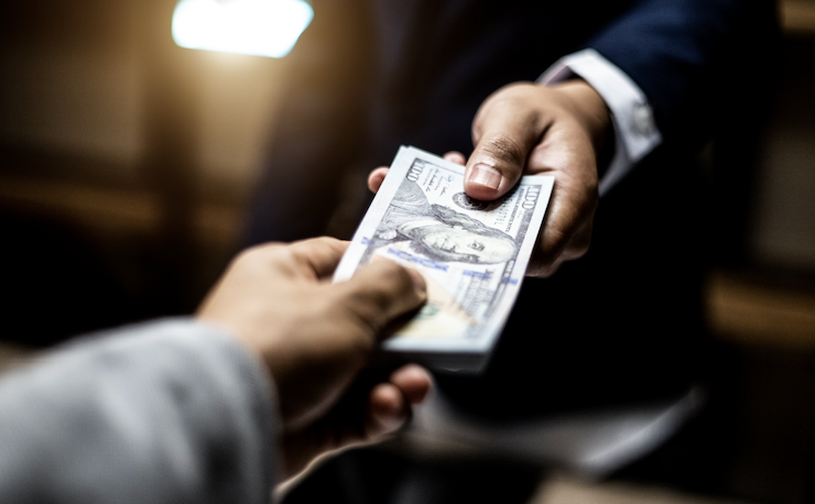 Closeup photo of the hand of a businessman passing a wad of 100 dollar bills to another