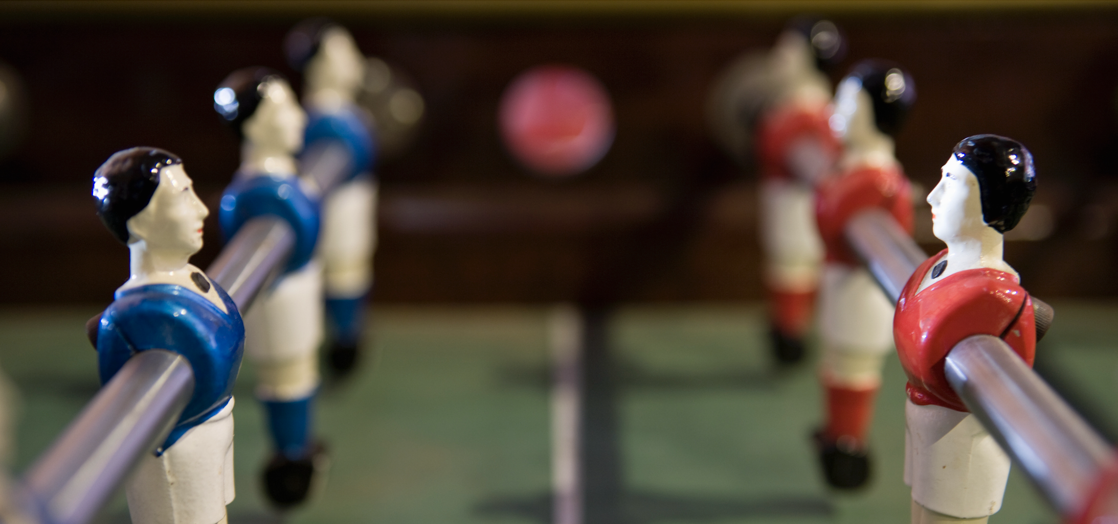 Closeup image of a foosball table, with plastic figures on metal rods facing off in blue and red jerseys.