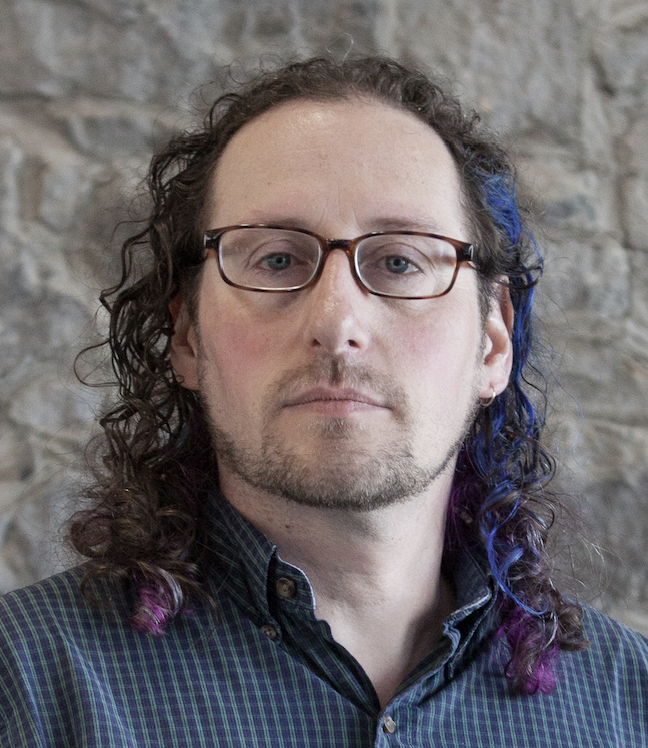 Author headshot. A White man in his 30s/40s with glasses and wisp of blue in his curly brown hair.