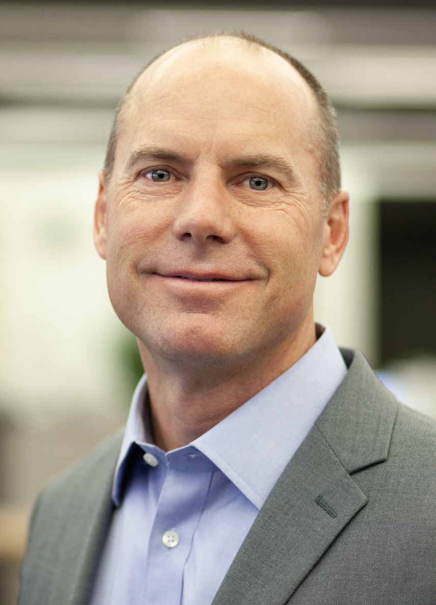 An image of a smiling bald White man in a crisp blue shirt and gray blazer.