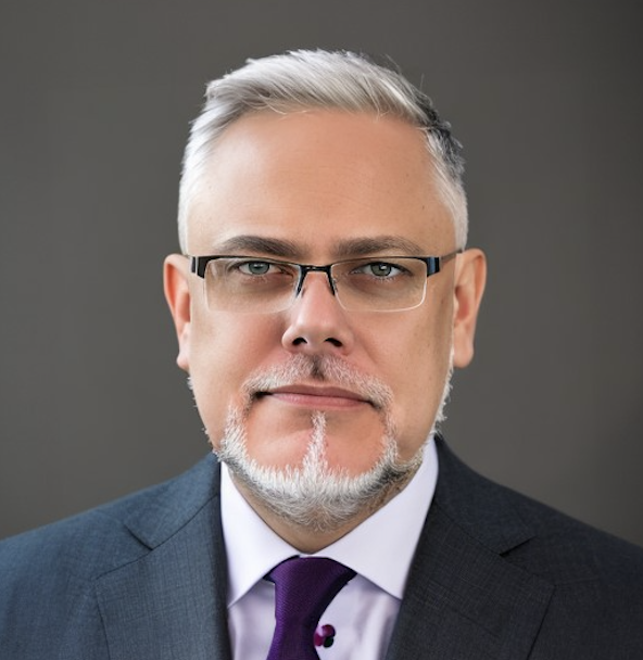 Photo of a white man in a suit with white hair, glasses, and a thin sculpted mustache and beard.