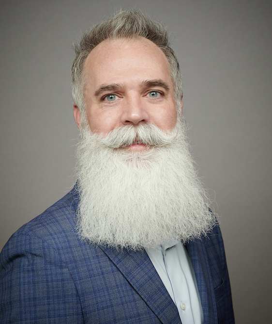 A photo of a middle-aged white man with blue eyes, graying hair, and an attention-getting white beard running halfway down his chest.