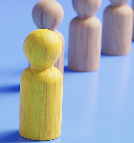Wooden figures stand in a diagonal line against a blue field, with one yellow figure one step forward.