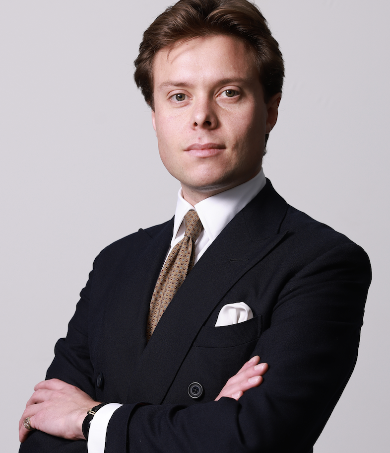 Photo of a 30something white man with brown hair, arms folded, wearing a crisp double-breasted navy suit.