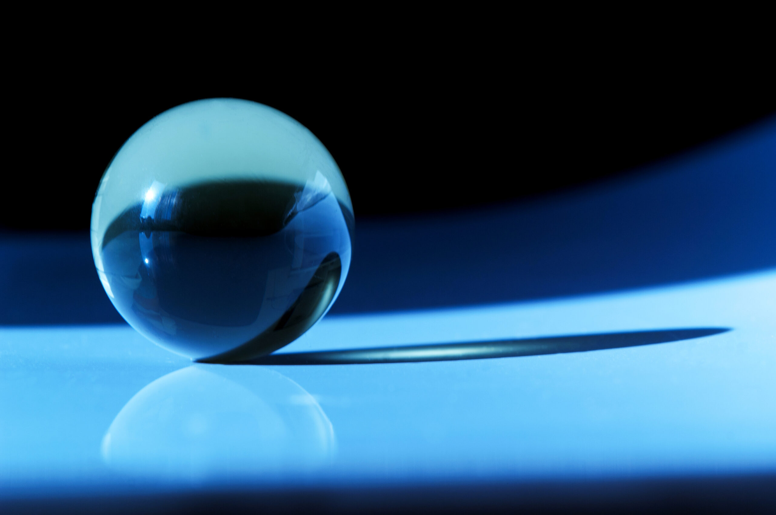 A photo of a crystal ball sitting on a glossy light blue surface against a black background.