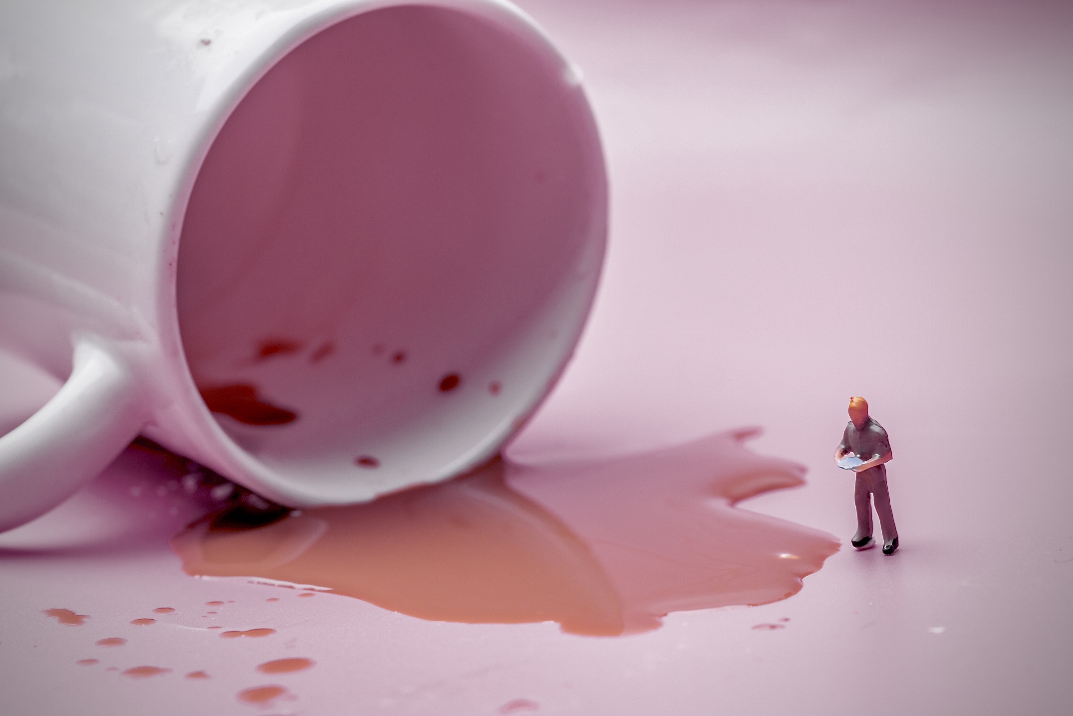 An image of a miniature human figure assessing spilled coffee from an overturned mug.