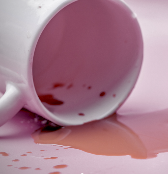 An image of a miniature human figure assessing spilled coffee from an overturned mug.