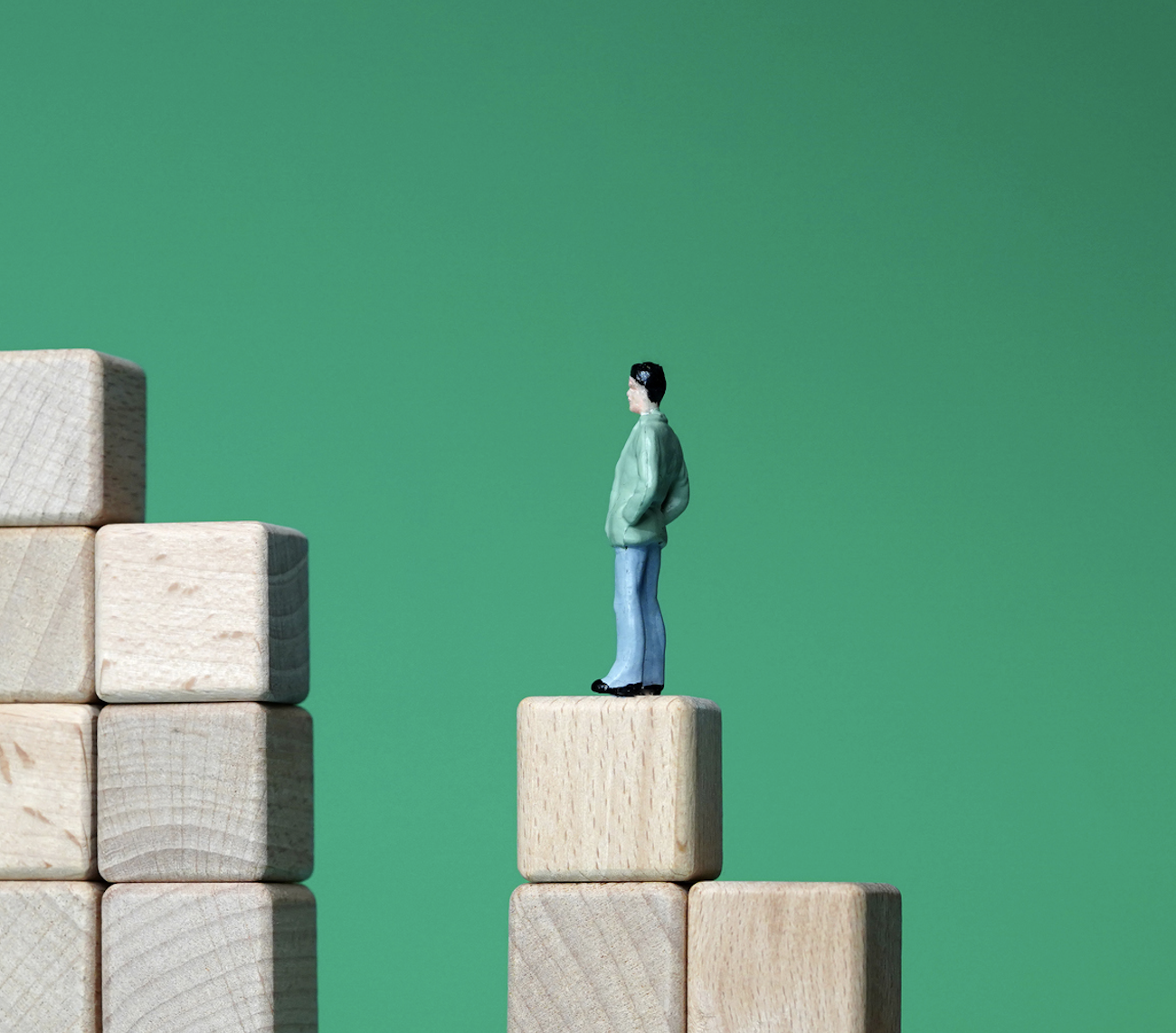 A photo of a small toy figure of a man standing on a staircase of blocks split by a large gap