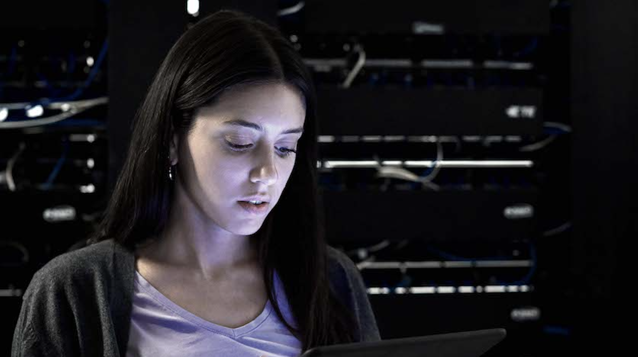 Photo of a young woman with long dark hair looking down at a laptop.