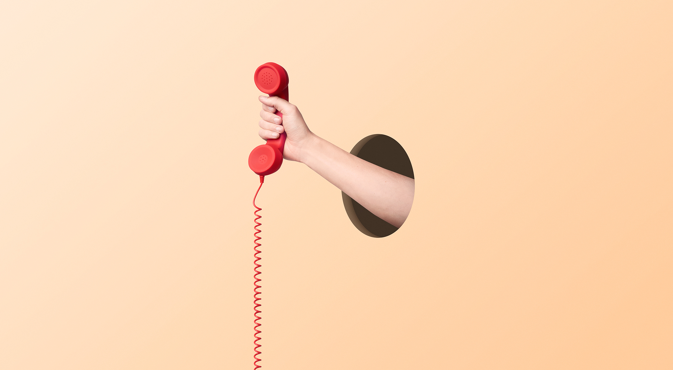 An image of a hand sticking trhough a wall and gripping a red corded phone receiver.