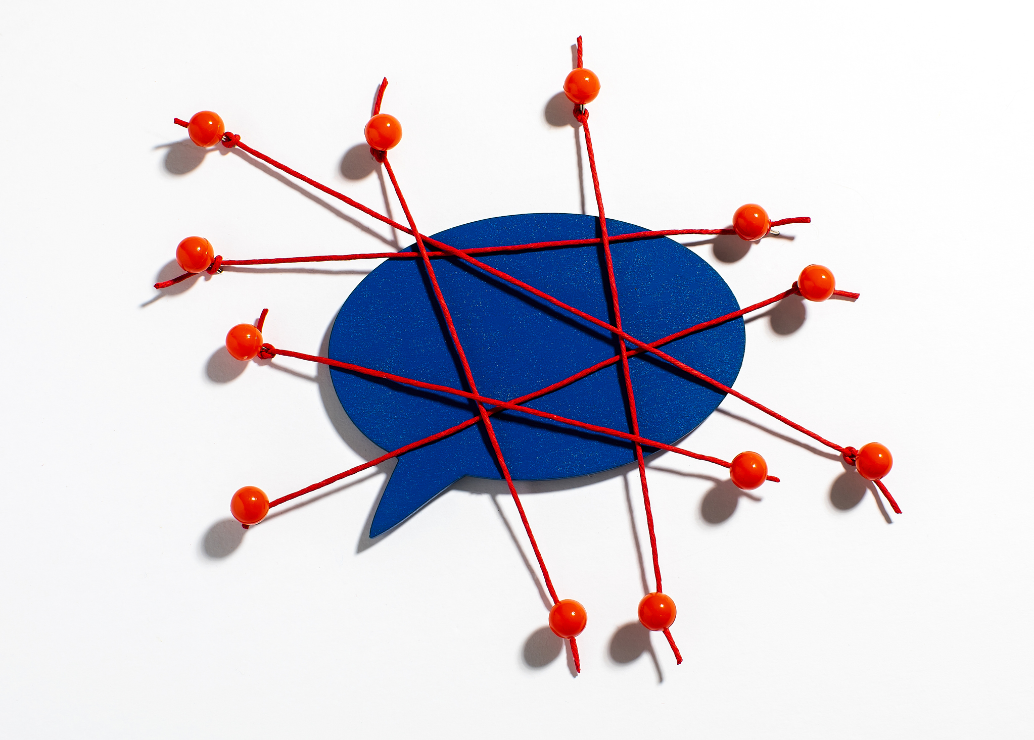 Image of a blue cartoon speech bubble wrapped in a web of red threads held down with pushpins.