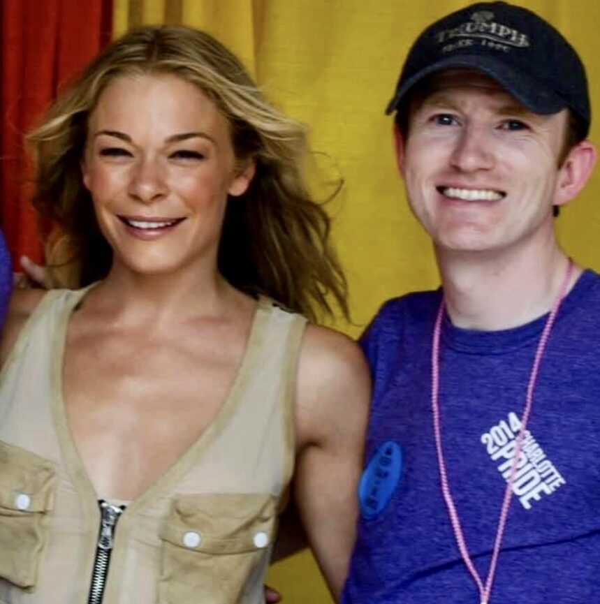 Photo of Paul Kelly with LeAnn Rhimes posed before a curtain