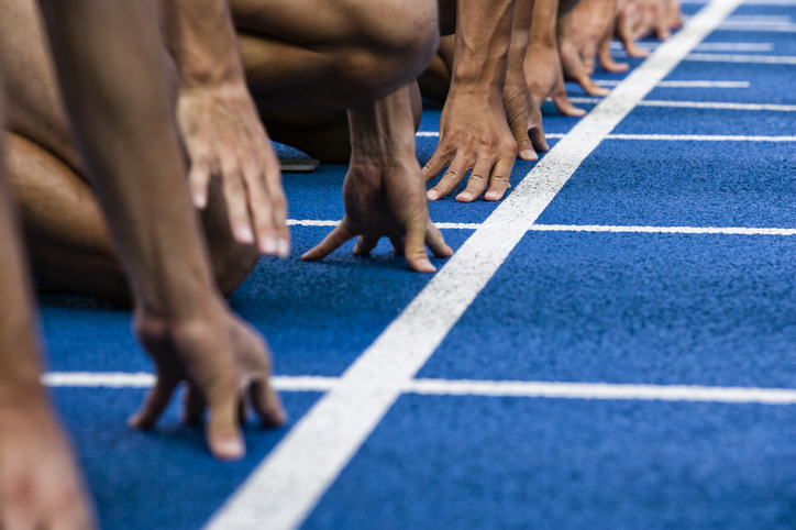 A closeup photo of runners' hands gripping the ground at the starting line of a race.