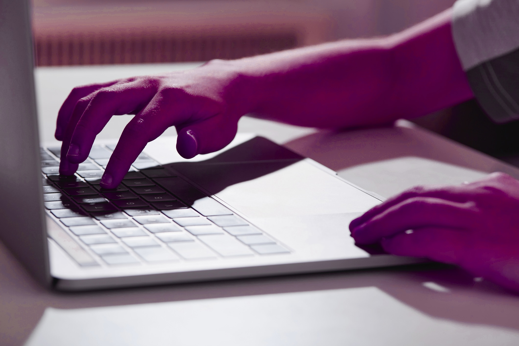 A hand and its dark shadow loom over a laptop keyboard.