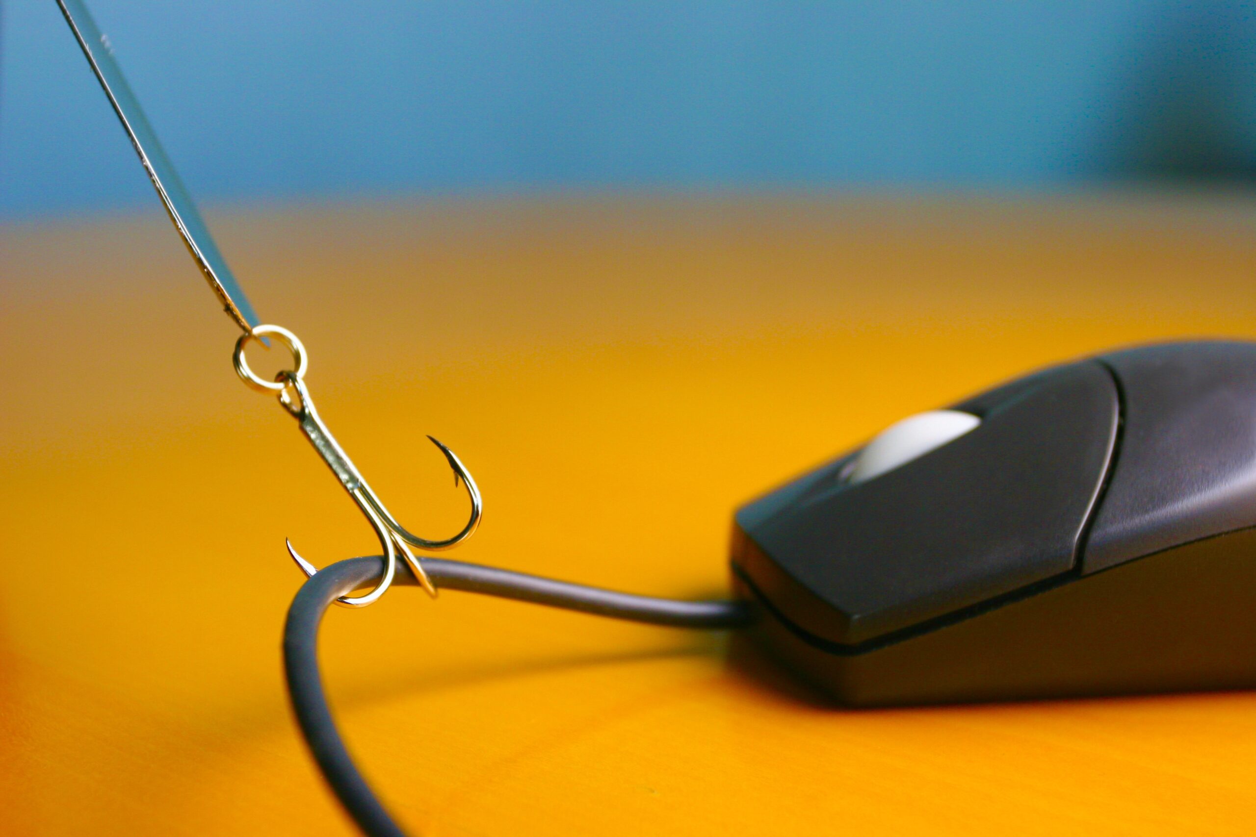 Photo of a fishhook catching the wire of a computer mouse on an orange desktop.